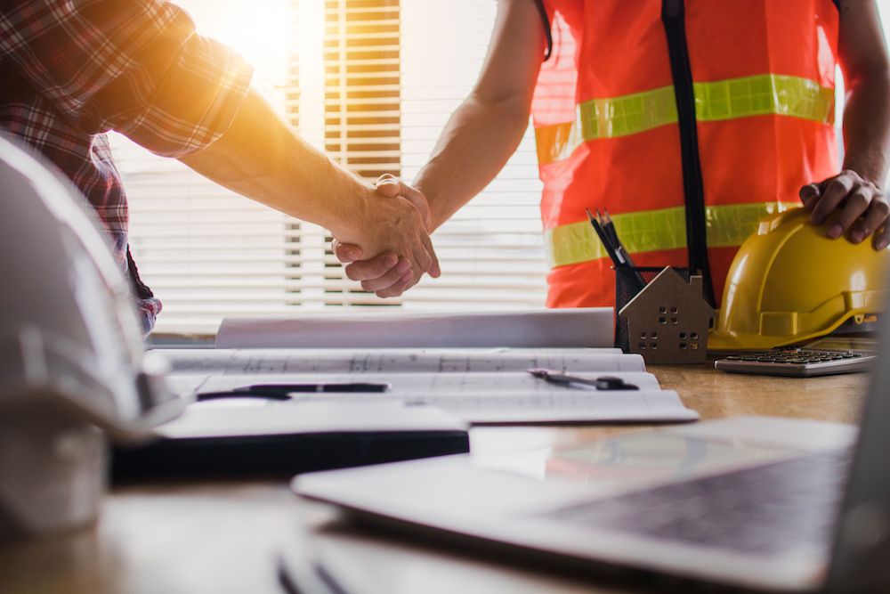 Un jefe y un obrero de la construcción se dan la mano en una oficina.